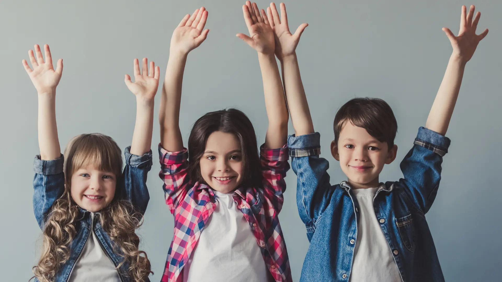 Three confident children raising their hands to participate